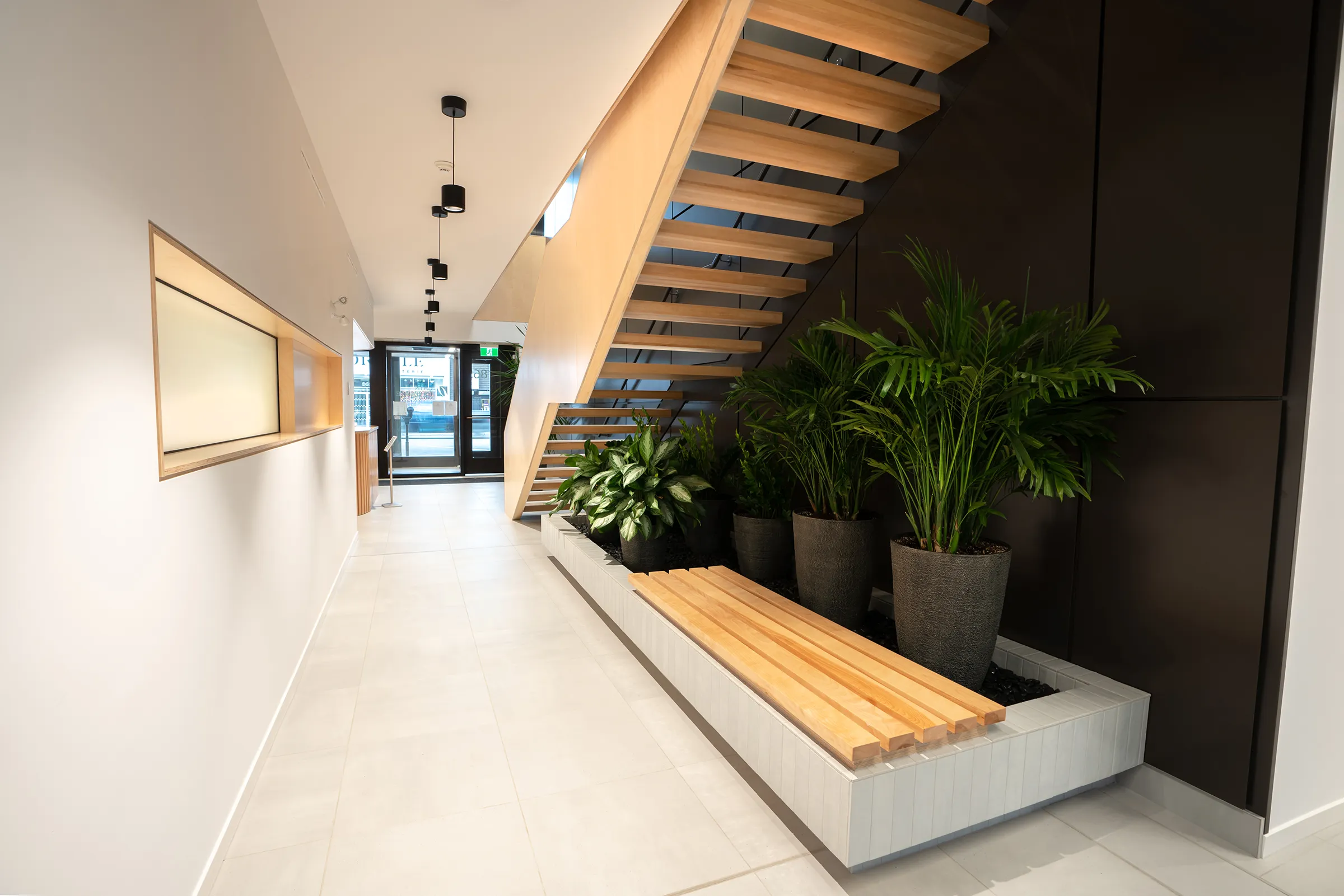 Vue intérieure d'un couloir sous un escalier avec un banc et des plantes